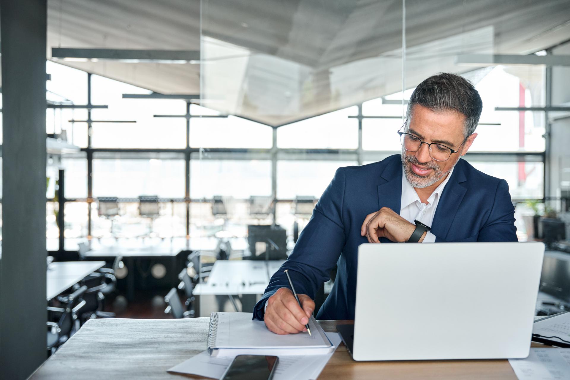 Hombre de negocios de mediana edad trabajando en una computadora portátil en la oficina escribiendo notas.